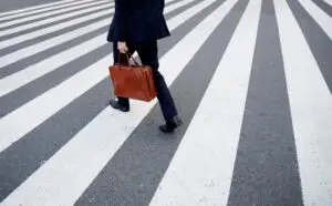 High angle view of person carrying brown briefcase walking across pedestrian crossing.